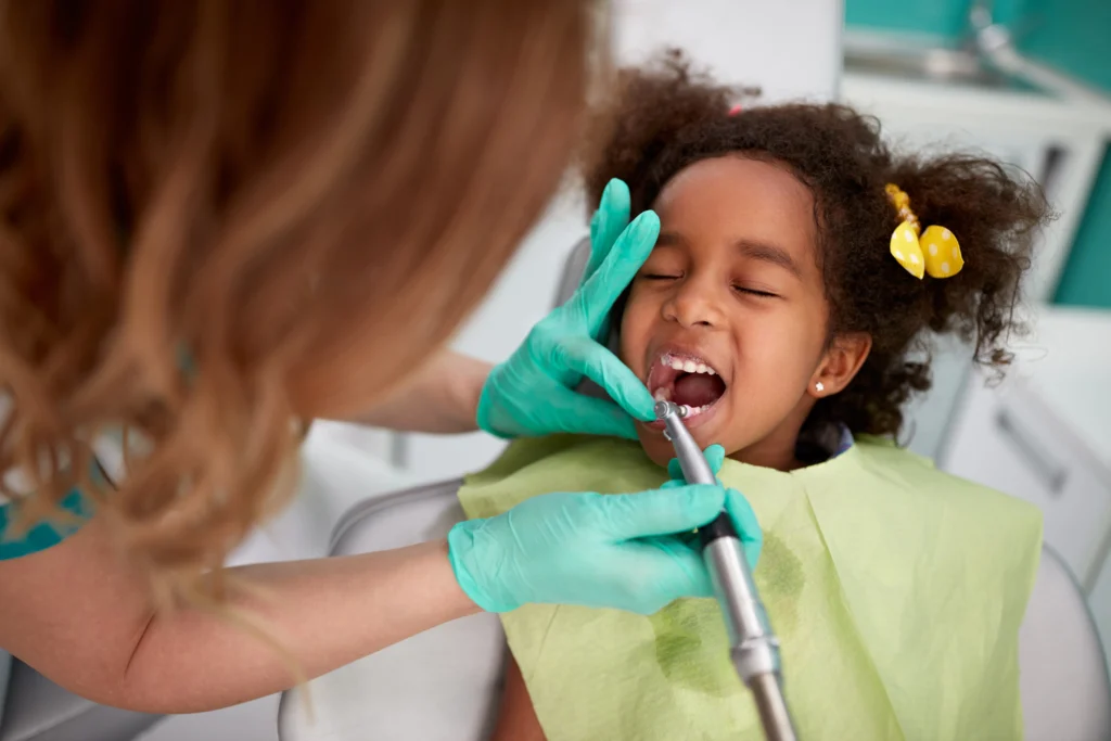Girl with bows in her hair getting her teeth cleaned by a dentist